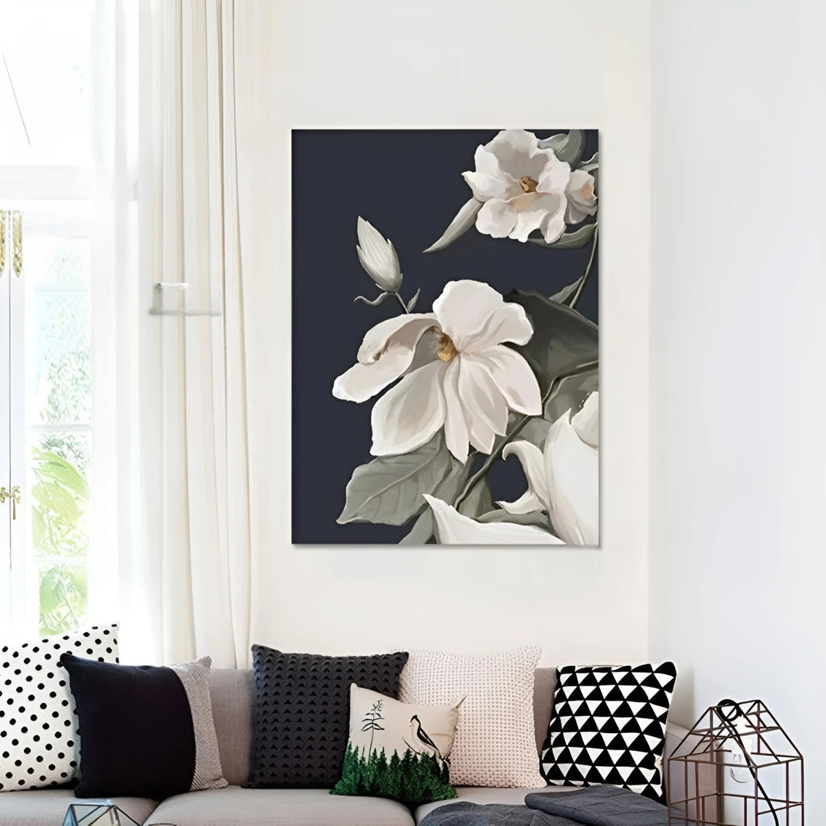 Framed floral painting with soft white petals and green leaves, displayed on a dark wooden wall above a modern beige sofa in a cozy living room.
